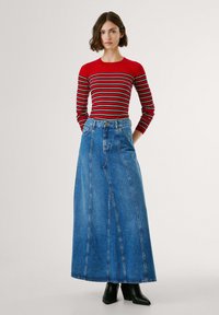 Rode en zwarte gestreepte ribbelsweater met lange mouwen, gecombineerd met een lange blauwe spijkerrok met zichtbare stiksels en zijzakken.