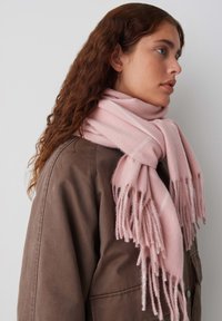 Pink scarf made of soft woven fabric, featuring fringed ends and subtle light stripes, draped around a person's neck.