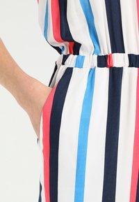 Randig jumpsuit med vertikala ränder i röd, blå, vit och marinblå. Mjuk tygkvalitet med elastisk midja och sidfickor.