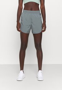 Pantalones cortos deportivos grises de tela ligera, con cinturilla elástica y bolsillos laterales, combinados con zapatillas blancas.