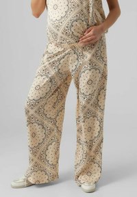 Beige mönstrade gravidbyxor i lättviktig tyg har en blommig design med vida ben och elastisk midja. Stylade med vita sneakers.