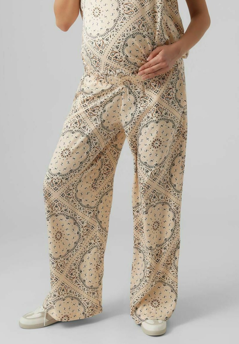 Beige mönstrade gravidbyxor i lättviktig tyg har en blommig design med vida ben och elastisk midja. Stylade med vita sneakers.