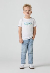 Άσπρο κοντομάνικο T-shirt με πολύχρωμο γραφικό "Levi's". Συνδυασμένο με ανοιχτό μπλε τζιν και άσπρα αθλητικά παπούτσια με μαύρες λεπτομέρειες.