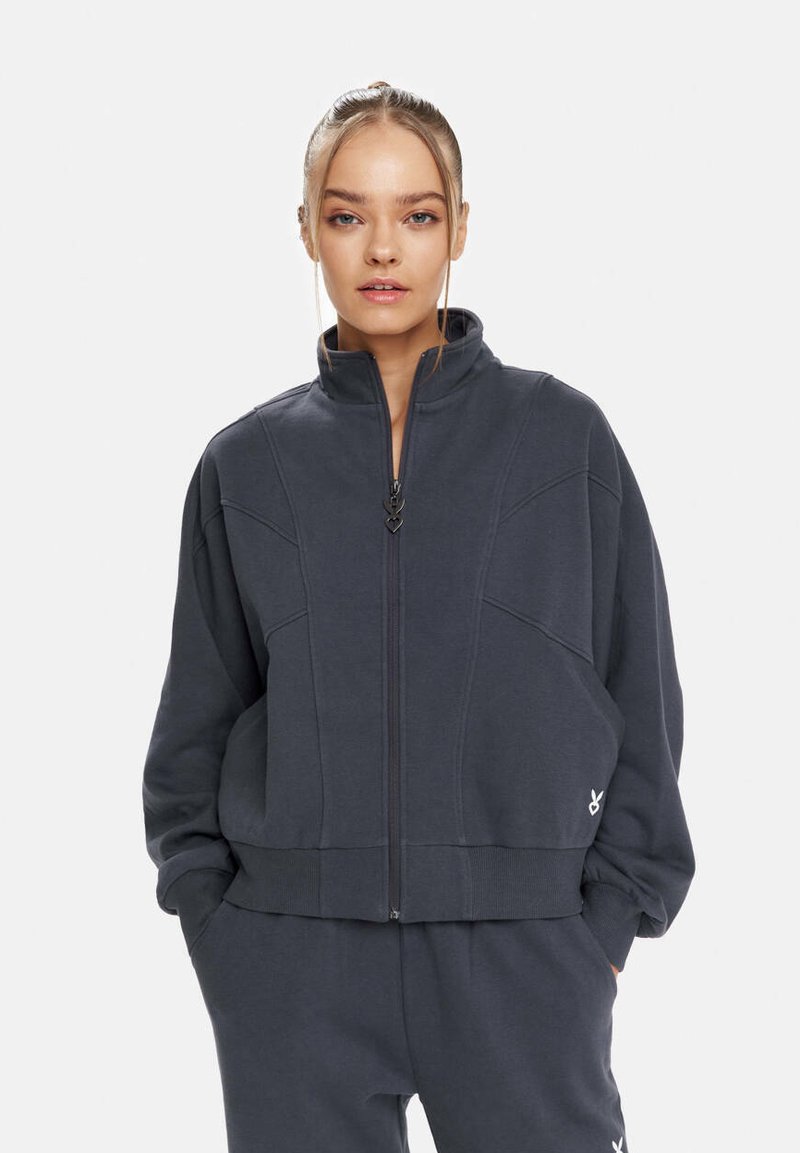 Grauem Zip-up Sweatshirt aus weichem Stoff, mit hohem Kragen, strukturierten Nähten, gerippten Bündchen und einem kleinen Logo-Akzent.
