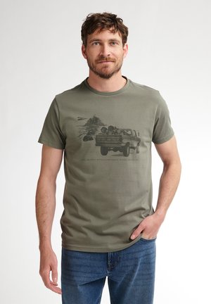 T-shirt en cotton vert olive à manches courtes, avec un graphique d'un camion et d'une scène de montagne en noir, col rond et coupe décontractée.