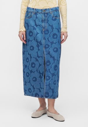 Jupe midi en denim avec motif floral bleu foncé, fente à l'avant, passants de ceinture, portée avec un haut à manches longues beige à fleurs et des chaussures plates beige clair.