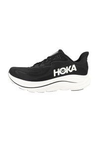 Chaussure de course noire avec une tige en mesh, logo HOKA blanc, semelle intermédiaire blanche épaisse, détails texturés, et semelle extérieure noire avec des rainures pour l'adhérence.