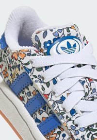 Floral-patterned sneaker in white, featuring blue leather stripes, white laces, and a blue logo patch; textured rubber sole.