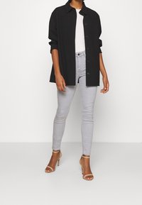 Camisa chaqueta negra de gran tamaño, blusa blanca ajustada, jeans gris claro de corte skinny y sandalias de tacón nude con tiras. Tejido texturizado, detalles de botones.