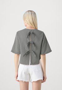 Kortärmad, svart och vit rutig topp med hög rygg, som har tre tygband längs ryggraden och en rak fåll.