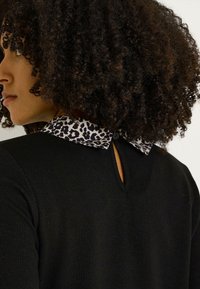 Top de punto negro con cuello de estampado de leopardo, cierre de botón en el cuello y un pequeño detalle de ojal en la parte posterior.