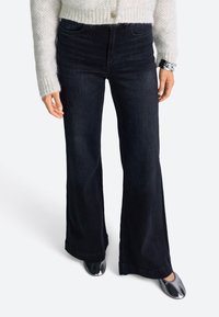 Črne flare jeans iz denima, z visokim pasom in temnim pranjem. V kombinaciji z lahkotno, teksturirano pleteno majico in metalnimi čevlji.