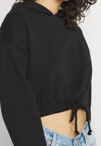 Sudadera corta negra con dobladillo ajustable, tela suave, diseño con capucha y corte relajado, combinada con pantalones cortos de mezclilla azul claros.
