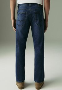 Jeans in denim blu scuro con un design a gamba dritta, con due tasche posteriori con pattine appuntite e una toppa in pelle marrone sulla cintura.
