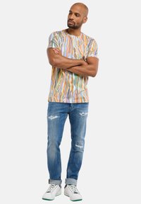 Multicolored short-sleeve t-shirt featuring a wavy pattern, paired with distressed light blue jeans and white sneakers with green accents.