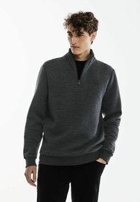 Grå kvartdragkedja tröja med texturerad tyg, ribbade muddar och nederkant, samt en liten logotyp på bröstet. Klassisk passform.