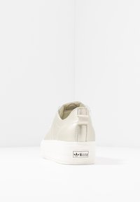 Krémově zbarvená teniska s hladkým koženým svrškem, texturovanými detaily, polstrovaným límcem a bílou podešví na platformě s logem.