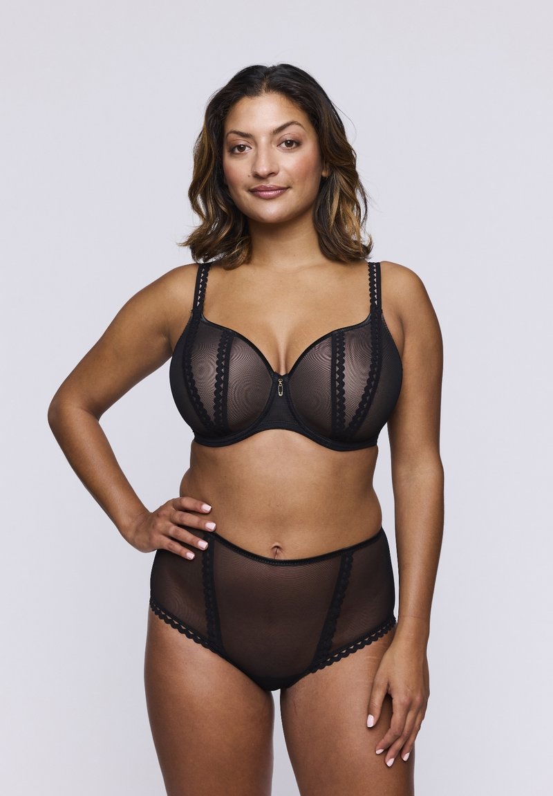 Conjunto de lencería negra que incluye un sujetador transparente con estampado y aros, junto con una braguita alta a juego. Destacados detalles de encaje decorativo.