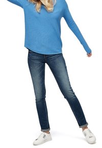 Chemise bleu côtelée à manches longues associée à un jean en denim bleu foncé et des baskets blanches. La tenue présente une coupe décontractée et une texture subtile.