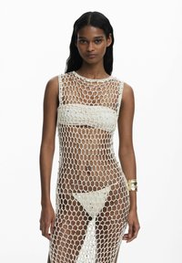 Dlhé, priesvitné biele šaty vyrobené z pletivovej tkaniny s geometrickým vzorom. Interiér obsahuje pevnú bandeau podprsenku a trojuholníkové nohavičky.