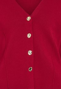 Cárdigan rojo de punto con escote en V, que presenta cinco botones dorados en la parte delantera y costuras sutiles para un diseño ajustado.
