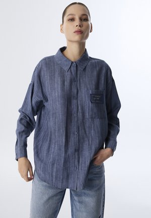 Blauw gestreepte overhemden met een kraag, voorzien van een opgestikte zak en een relaxte pasvorm, gecombineerd met lichtblauwe jeans. Gladde stoffen textuur.