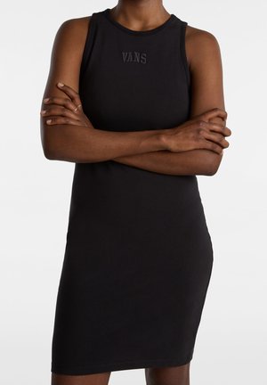 Osoba z założonymi skrzyżowanymi rękami, ubrana w czarną sukienkę Vans bez rękawów z logo na piersi, na tle jasnego, jednolitego tła.