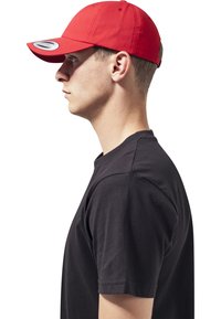 Rode pet met een gebogen rand, gemaakt van katoen. Draagt een zwart T-shirt met korte mouwen, weergegeven vanuit zijprofiel.