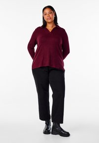 Maglione a collo in maglia bordeaux, con un motivo a coste testurizzato. Abbinato a pantaloni neri e stivaletti neri.