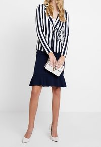 Marinblå och vit randig kavaj med en enkel knäppning, ihop med en marinblå utsvängd kjol. En vit handväska och klackar fulländar looken.