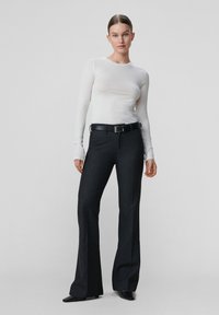 Hvid skjorte med lange ærmer kombineret med mørke, højtaljede viddebukser og et sort bælte, der har en glat tekstur og en skræddersyet pasform.