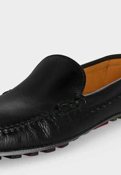 Mocassin en cuir noir sans lacets avec couture détaillée et doublure intérieure beige, montrant la vue de dessus et de côté.