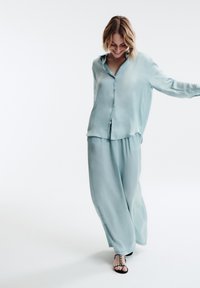 Camicia button-up di seta azzurro chiaro con maniche lunghe e pantaloni larghi coordinati. Texture liscia, leggero lucido, vestibilità rilassata e bottoni sulla camicia.