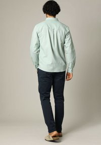  Lichtgroen overhemd met lange mouwen en knoopmanchet, relaxte pasvorm, gecombineerd met donker marineblauwe broeken en beige loafers, gezien vanuit de achterkant.