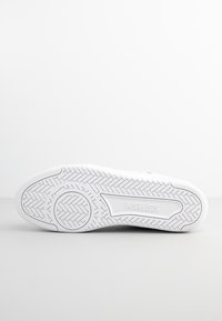 Bílá podrážka tenisky s texturovaným vzorem rybí kosti. Obsahuje kruhový design a embosované logo "KSWISS". Čistý, minimalistický design.