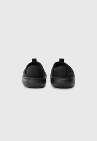 Svarta slip-on-skor med rundad form, tillverkade av mjukt material. Har en texturerad gummisul och en bakre dragflik för enkel påtagning.