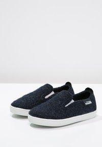Scarpe slip-on in feltro blu navy con suola in gomma bianca. Presentano pannelli laterali elasticizzati e un'etichetta con logo. Texture morbida con una forma arrotondata.