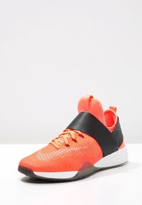 Scarpe sportive con una parte superiore in mesh arancione brillante, una fascia nera e una suola bianca. Presentano un motivo testurizzato e dettagli con lacci.