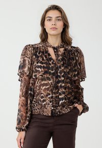 Blouse imprimée marron avec des volants superposés, un détail de nœud au cou et des manches longues. Elle présente un motif semblable à celui d'un léopard et un tissu légèrement transparent.