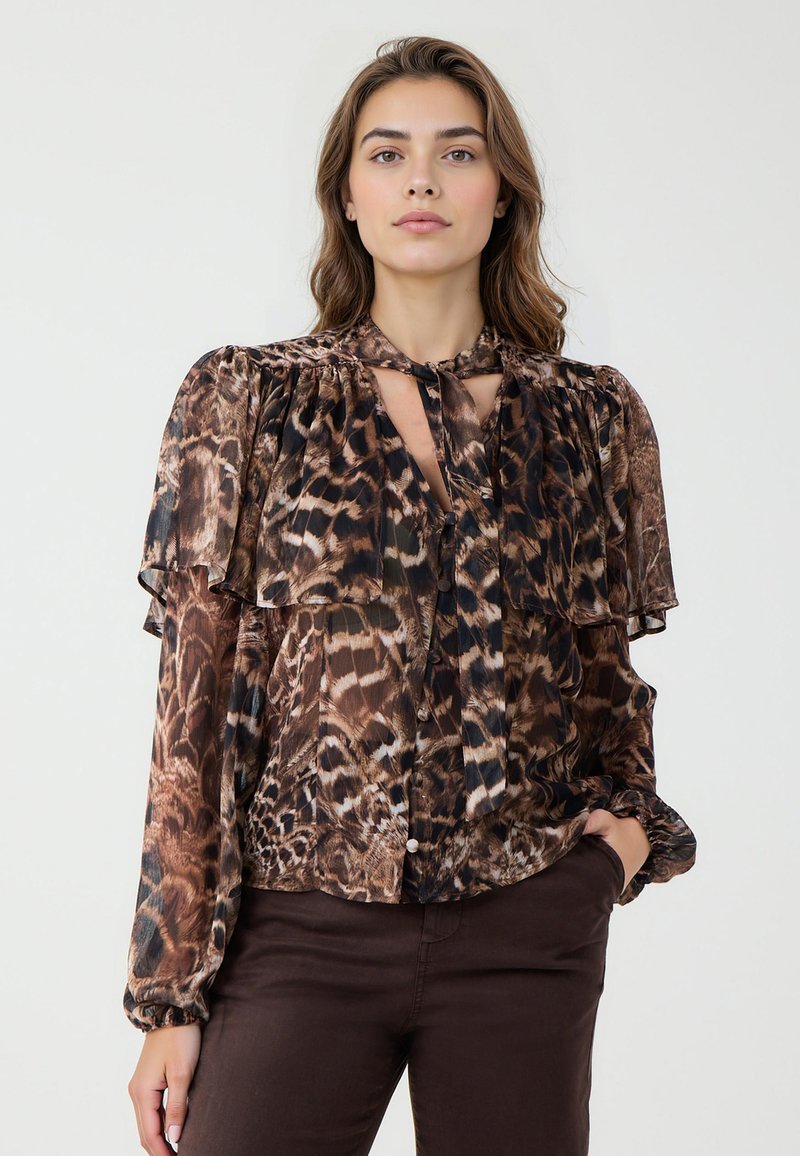 Blouse imprimée marron avec des volants superposés, un détail de nœud au cou et des manches longues. Elle présente un motif semblable à celui d'un léopard et un tissu légèrement transparent.