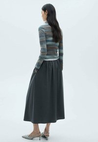 Flerfärgad randig stickad topp med långa ärmar, i kombination med en mörkgrå maxikjol. Skor: ljusgrå klackar. Släta texturer.