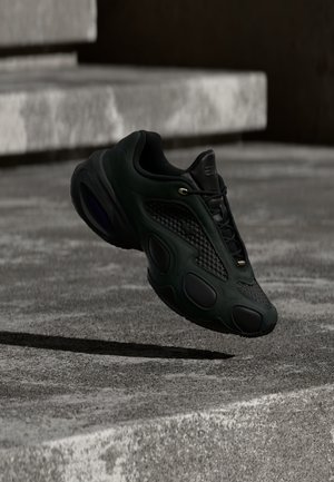 Μαύρο αθλητικό παπούτσι με υφασμάτινες επιφάνειες και κορδόνια που αιωρείται πάνω από μια τσιμεντένια επιφάνεια και σκάλες σε χαμηλό φωτισμό.