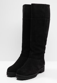Černé semišové kozačky po kolena s kulatou špičkou, plochou podrážkou a minimálními švy na hladkém povrchu.