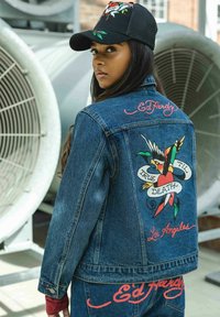 Chaqueta de mezclilla con un diseño de tatuaje bordado colorido en la parte posterior, que incluye "True 'Til Death" y "Los Ángeles", con acentos de texto en rojo.