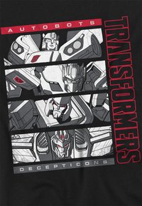 Schwarzes T-Shirt mit einem Grafikdesign, das Autobots und Decepticons aus Transformers in Grau und Rot zeigt, mit roboterhaften Gesichtern und mechanischen Details.