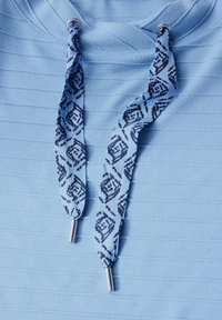 Světle modrá mikina s kapucí s ribovanou texturou, s pestrými stahovacími šňůrkami tmavě modré barvy a stříbrnými kovovými konci.