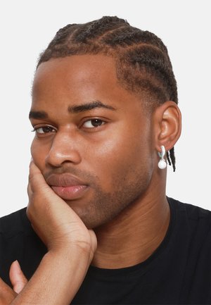 Silver hoop earring with a white pearl accent. Subject has braided hair and a neutral expression, wearing a black shirt. Clear background.