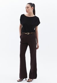 Mustat lyhyet hihatut paidat, ruskeat leveälahkeiset housut halkioilla, leopardikuvioinen vyö ja mustat korolliset sandaalit. Sujuva kankaan rakenne.