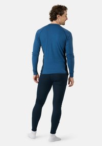 Chemise à manches longues bleu canard côtelée avec des panneaux latéraux foncés contrastants, associée à des leggings foncés ajustés. Chaussettes blanches visibles au niveau des chevilles.