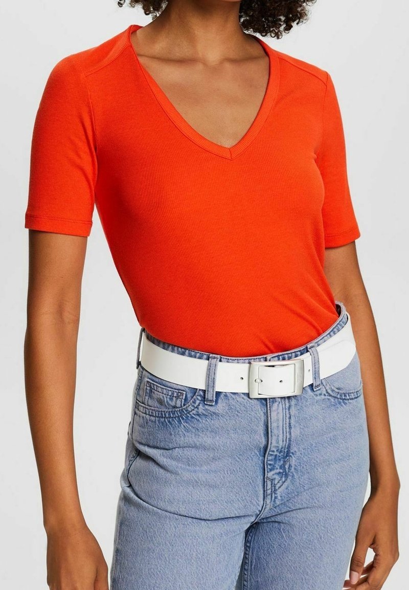 Haut rouge à manches courtes côtelé avec col en V, associé à un jean en denim bleu clair et une ceinture blanche avec une boucle argentée.